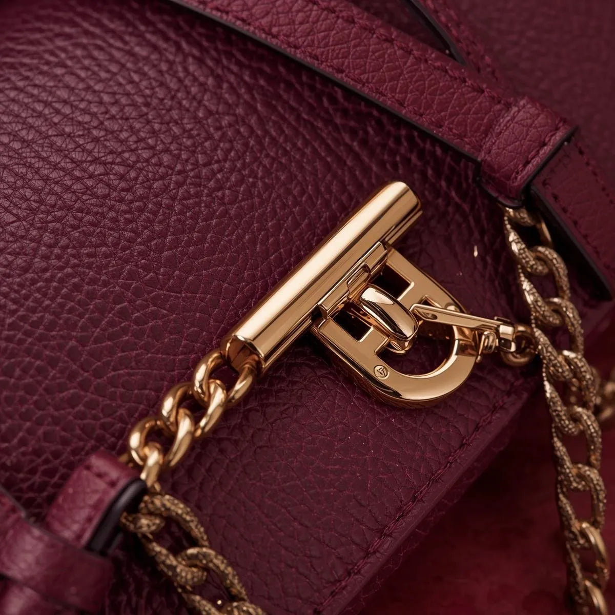 Close-up of a burgundy handbag with a gold chain and clasp.