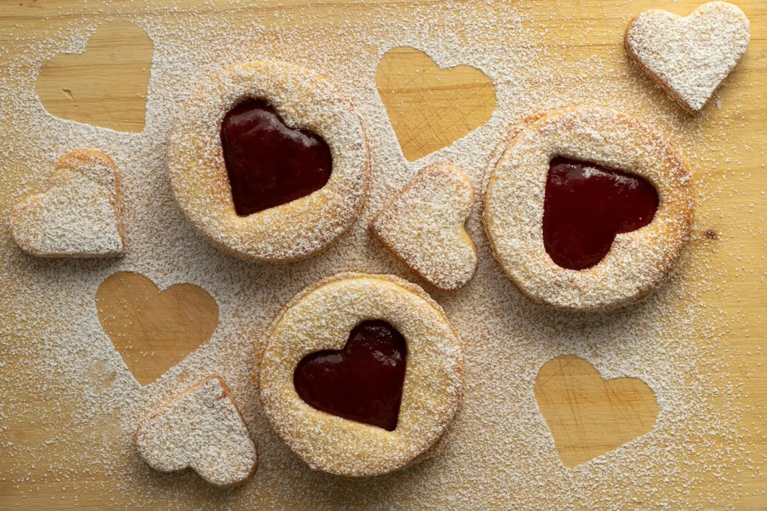 Delicious heart-shaped raspberry jam cookies, dusted with powdered sugar on a rustic wooden board.